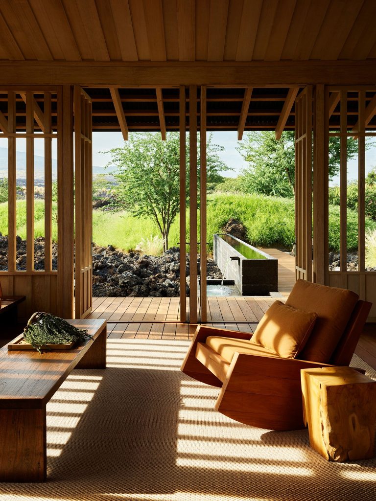 Open wood pavilion with a lounge chair looking out to a water trough and green landscape.