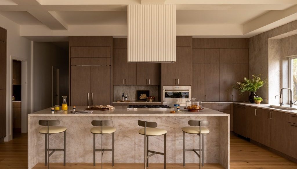 Kitchen with walnut cabinetry, a quartzite waterfall island and four counter stools in warm light.