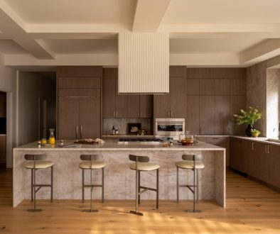 Kitchen with walnut cabinetry, a quartzite waterfall island and four counter stools in warm light.