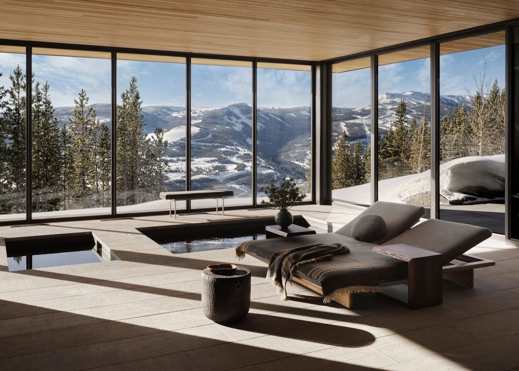 Mountain spa room with soaking pools, a chaise lounge and floor-to-ceiling windows over snowy peaks.