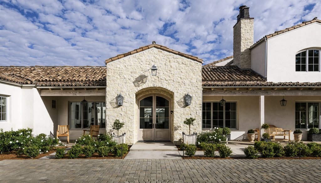 Estate front facade with an arched stone entry, clipped hedges and a cobblestone drive