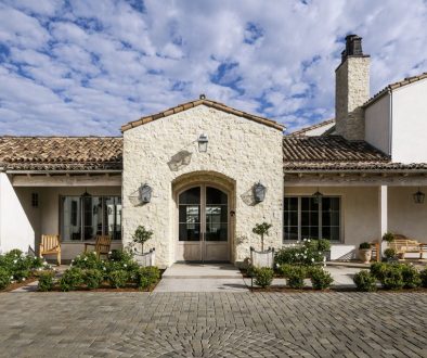 Estate front facade with an arched stone entry, clipped hedges and a cobblestone drive