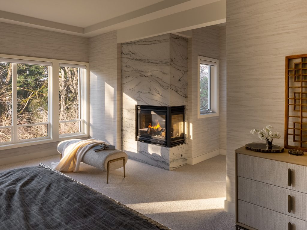 When Should You Hire an Interior Designer for a Custom Home? 2 Primary bedroom at golden hour with a corner marble fireplace and forest views